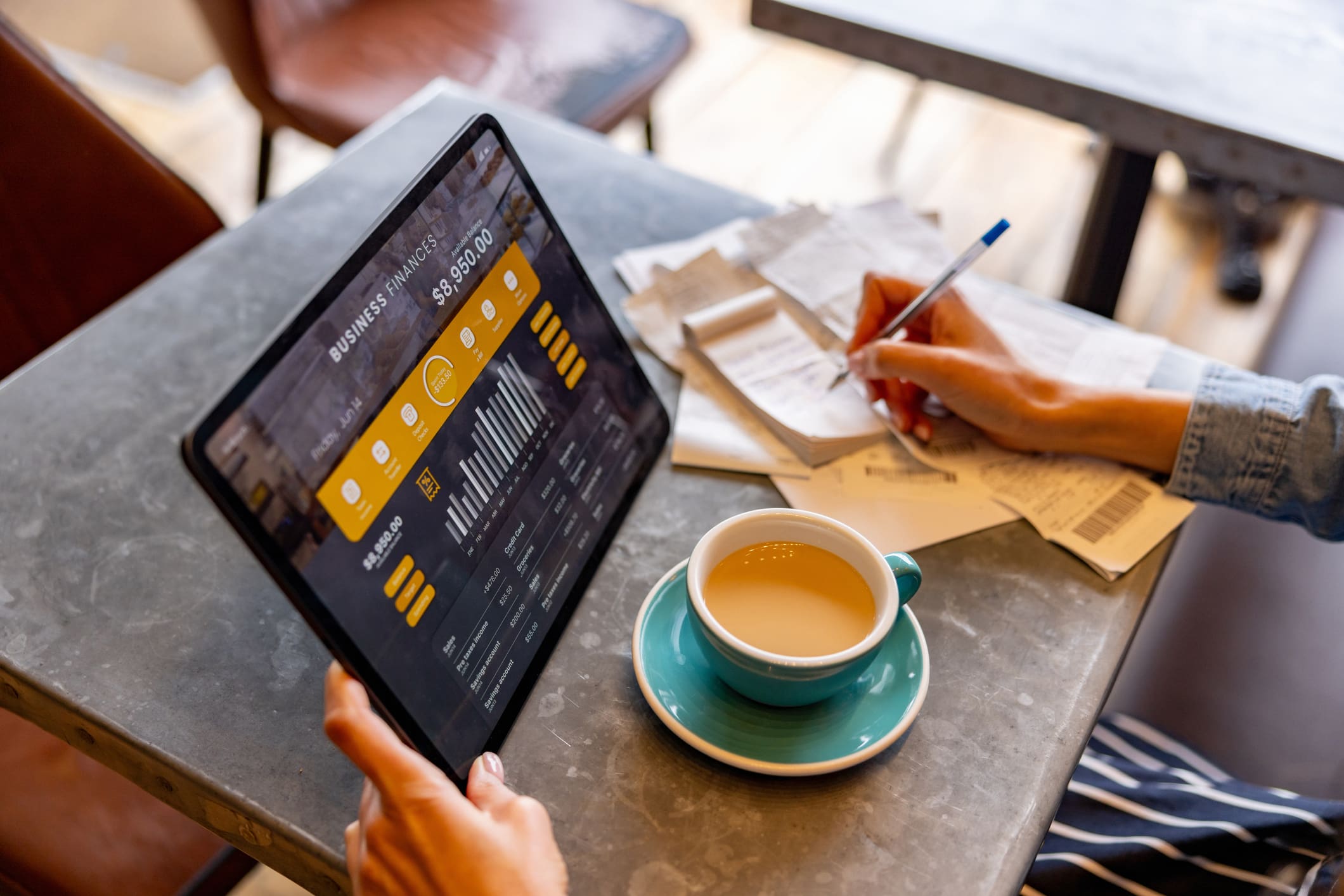 Tablet with graphs, person writing, coffee cup.