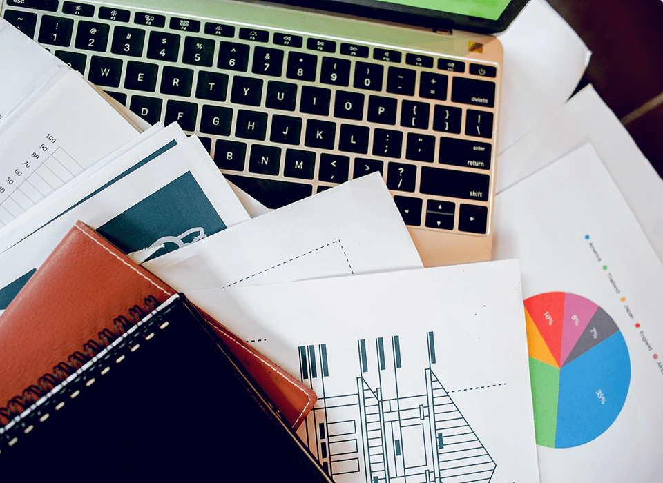 Laptop with documents and charts on desk.